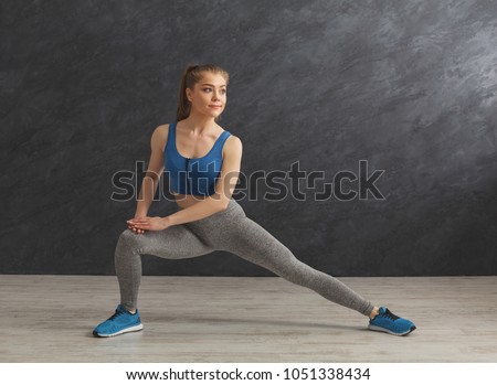 Fitness woman warmup stretching training at gray background indoors. Young slim girl makes aerobics exercise, copy space