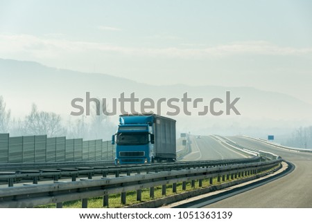 Blue lorry truck driving on asphalt highway road with protective fences in a rural landscape