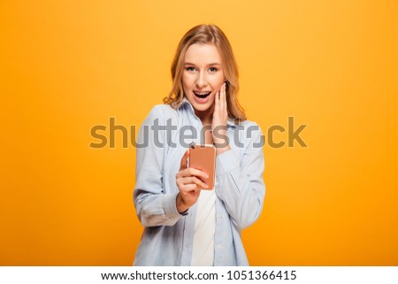 Portrait of a happy young girl with braces holding mobile phone isolated over yellow background