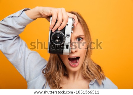 Close up portrait of an excited young girl with braces taking a picture with photo camera isolated over yellow background