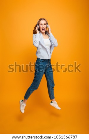 Image of cheerful young lady jumping listening music isolated over yellow background looking camera.