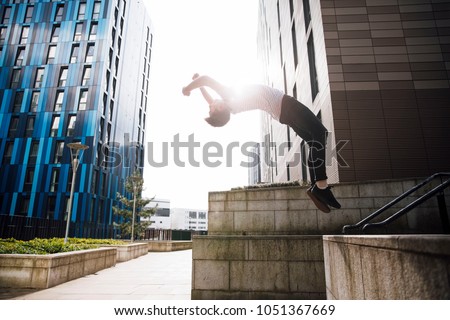 Freerunner is doing a backflip off a wall in the city.  Royalty-Free Stock Photo #1051367669