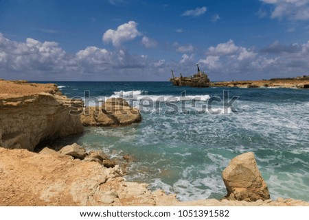Shipwreck. Ship on the rocks near the shore - turquoise sea with waves  on  background of   cloudy sky. Cliffs  in water. The Mediterranean coast near Paphos, Cyprus. Maritime landscape. 