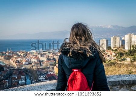 City of Rijeka view from Trsat, Kvarner bay of Croatia.
View from above on the city and harbor of Rijeka, Croatia, girl with red backpack in foreground.
 Royalty-Free Stock Photo #1051393652
