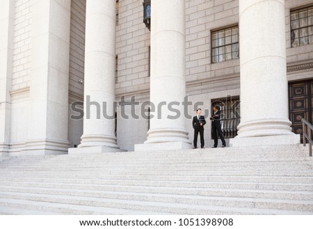 A well dressed man and woman converse on the steps of a legal or municipal building. Could be business or legal professionals or lawyer and client. Royalty-Free Stock Photo #1051398908