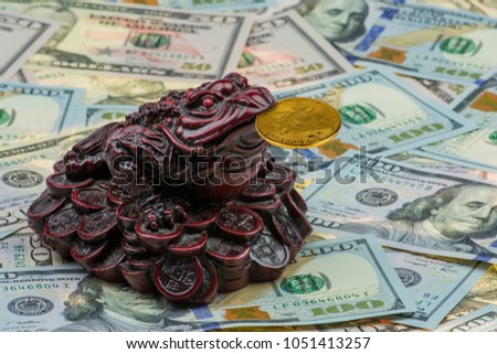 three-legged money toad Jin Chan as a chinese symbol of wealth with gold bitcoin in mouth on variety of US hundred-dollar and fifty-dollar bills. New virtual money. Crypto currency 