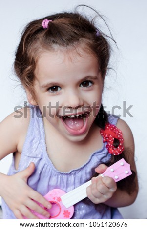 Happy little girl having fun playing with toy guitar or ukulele.