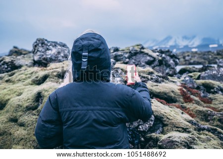 Girl holding phone in her hands with her back view with the lava green moss on the background in Iceland