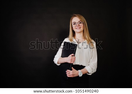 Studio portrait of blonde businesswoman in glasses, white blouse and black skirt holding laptop against dark background. Successful woman and stylish girl concept.