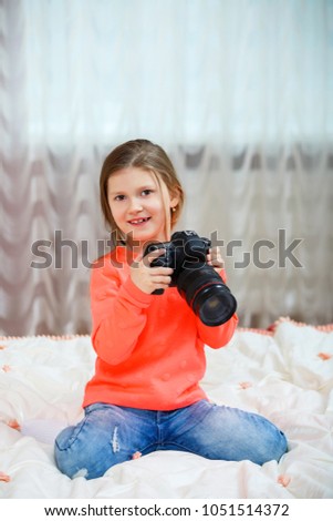 beautiful happy little girl sitting on bed and using a camera. Home, indoors concept. Lifestyle