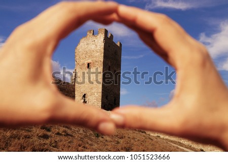 The corner tower of an old stone fortress, a picture through a window formed by folded palms.