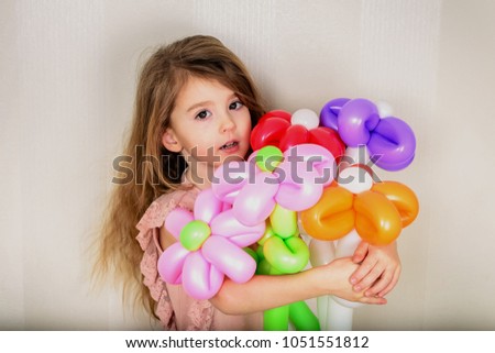 brown-eyed girl with unbuttoned hair hugs with both hands a large bouquet of flowers from inflatable balls of red, orange, pink and lilac