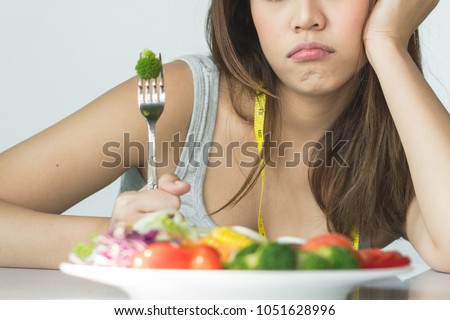 unhappy asian women is on dieting time looking at broccoli on the fork. girl do not want to eat vegetables and dislike taste of broccoli. Royalty-Free Stock Photo #1051628996