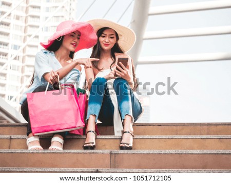 Two beautiful young women sitting on the stairs and using smart phone after enjoying in shopping