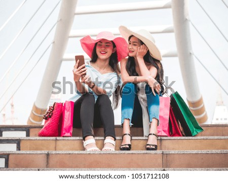 Two beautiful young women sitting on the stairs and making self-portrait by smart phone after enjoying in shopping