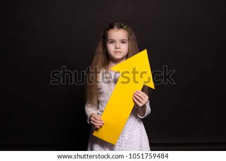 portrait of young caucasian girl with big yellow arrow, shot in studio on black background