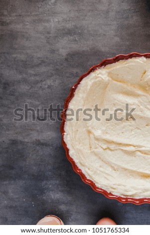 Butter in a red round ceramic tart baking pan. Making pie concept. Minimal dark food photography styling. Vertical, flat lay. Copyspace for text