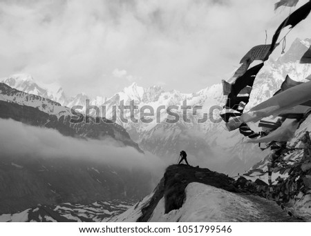 Tiny man Take Photo Among Snow Cover Huge Mountain on Annapurna Base Camp and Nepal Flag Against Wind in Black and White 