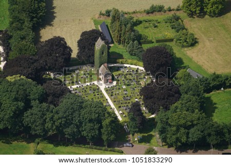 Aerial view of a old church tower covered with green ivy in Hoogzand Oostermeer, Friesland, Holland. It stands on a circle shaped cemetery surrounded by large trees.