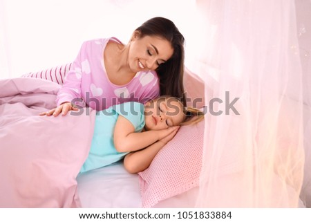 Mother looking at her cute daughter sleeping in bed at home
