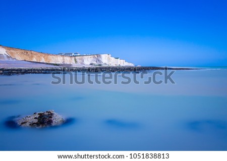 Peacehaven cliffs in East Sussex, United Kingdom. South Coast costal blue sea and sky. Long exposure picture, beach scene with Mediterranean like sea. Seascape from a boat, rock in the foreground.