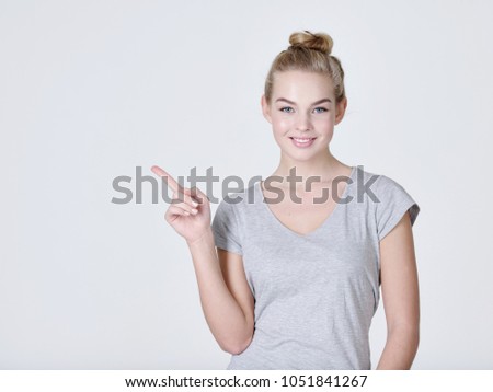 Smiling pretty woman pointing finger away over gray background. Looking at camera
