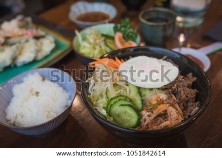 Korean Bi bim bap dish with rice, cucumber, beef,kochujang sauce, bean sprouts and carrots in a delicious meal on a table with other asian food served in the background.
