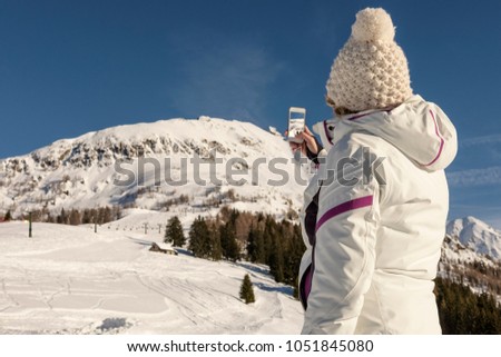 young woman with ski clothes take a picture of the mountain view with phone