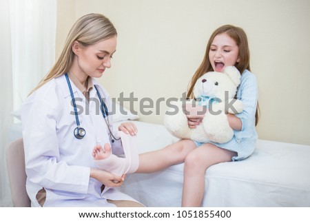 Doctor woman bandaging wound around little girl's leg and foot. Pediatrician doctor bandaging child's leg. Healthcare and medical young children concept.