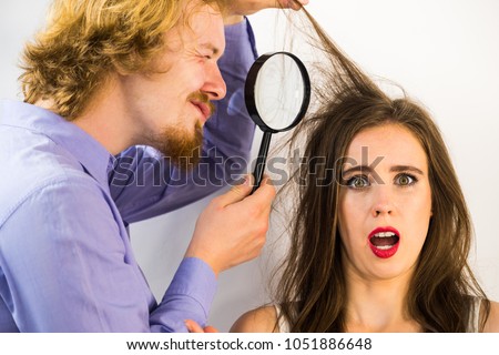 Man looking at woman hair using magnifying glass. Female looking unhappy having some haircare problems, split ends or lice