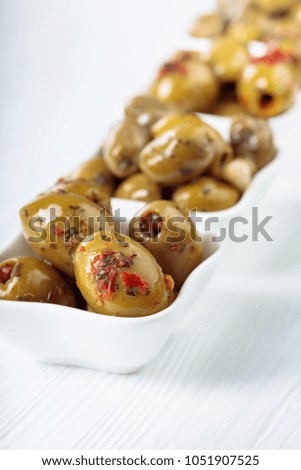 Spiced green olives in oil on a white wooden table. 