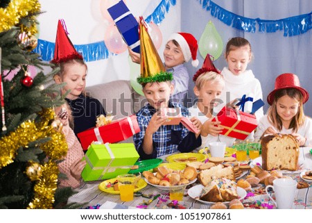 Boys and girls giving gifts to each other during Christmas dinner in home
