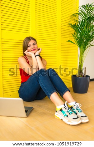 Attractive stylish girl with a laptop on a background of yellow wall.