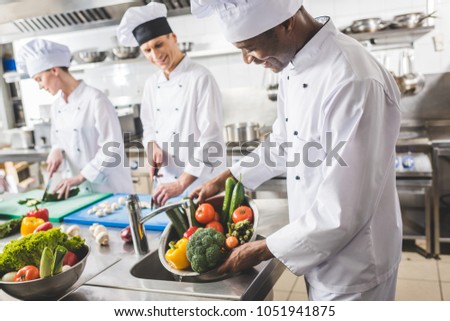 smiling african american chef washing vegetables at restaurant kitchen