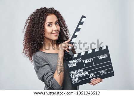 Smiling curly female holding movie clapper board, slate film.
