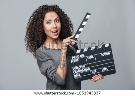 Smiling surprised curly female holding movie clapper board, slate film.