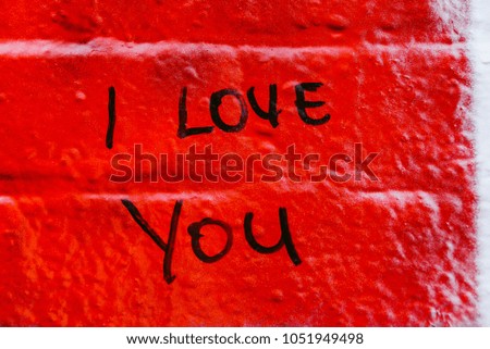 Red painted urban brick wall with romantic i love you message written at it in black color