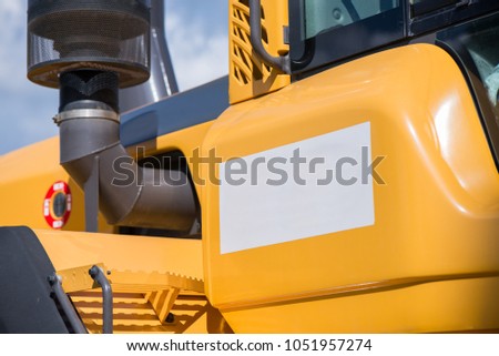 Space for text or logo. Side of yellow excavator. Road construction workers repairing highway road on sunny summer day. Loaders and trucks on newly made asphalt. Heavy machinery working on street.