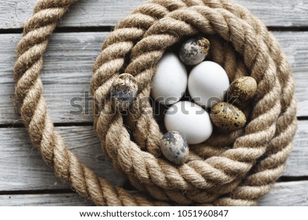 Chicken and quail's eggs in the nest made of rope on wooden background