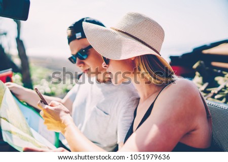 Male and female tourist reading map and using navigation app on smartphone for searching route sitting in rental car, couple of travelers browsing information on cellphone for getting to destination