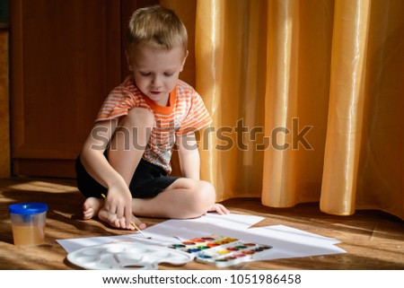 Little boy 3 years draws paints sitting on the floor of the room