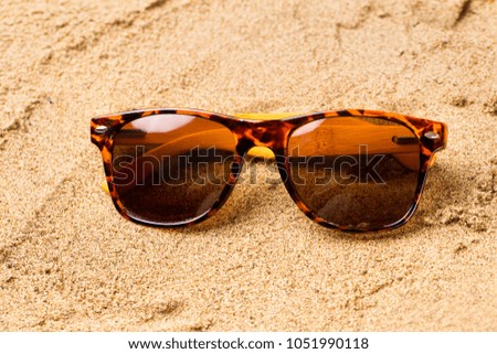 Closeup image of femalle brown sunglasses at sea yellow sand background.