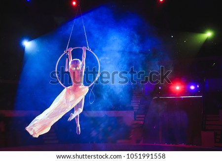 Aerial acrobat in the ring. A young girl performs the acrobatic elements in the air ring. Royalty-Free Stock Photo #1051991558