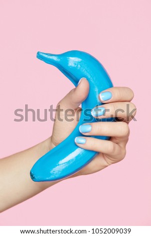 Nails Beauty. Hand With Blue Nails Holding Banana Fruit. Close Up Of Woman Fingers With Color Art Manicure And Blue Banana On Pink Background. Design For Nails. High Resolution.