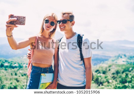 Cheerful hipster guy smiling making picture with girlfriend on smartphone camera resting on journey together, romantic couple taking selfie on natural landscape scenery  traveling on vacations