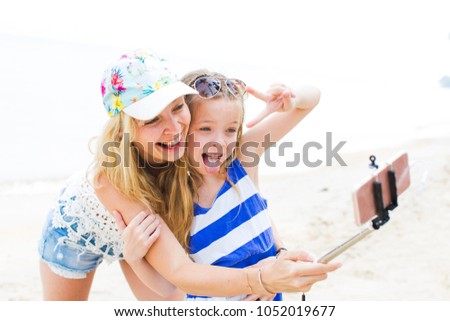 beautiful mother and her cute daughter doing a selfie photo with her phone on a beach in thailand