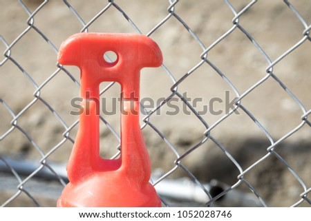 Macro close up on an orange plastic street cone and post with reflective silver tape, in front of a chainlink fence at a construction site