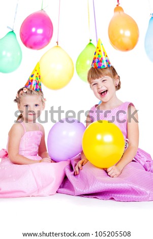 Laughing little girls in party hats holding balloons in hands