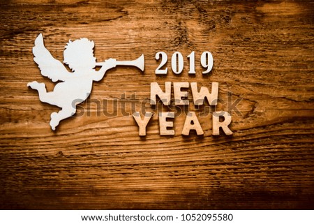 Wooden angel hold in hands wooden star on brown wooden background, merry christmas words, 2019 happy new year, minimalistic design