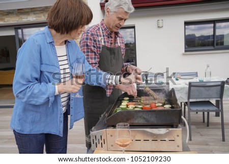 Senior couple preparing grilled meat on barbecue